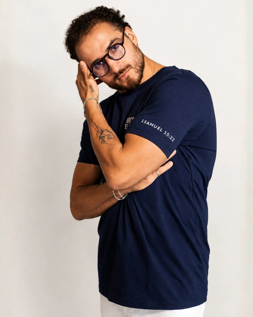 A man wearing a navy blue short-sleeve t-shirt with 'JERUSAL, 15:21' printed in white on the left chest and right sleeve, posed against a plain off-white background.