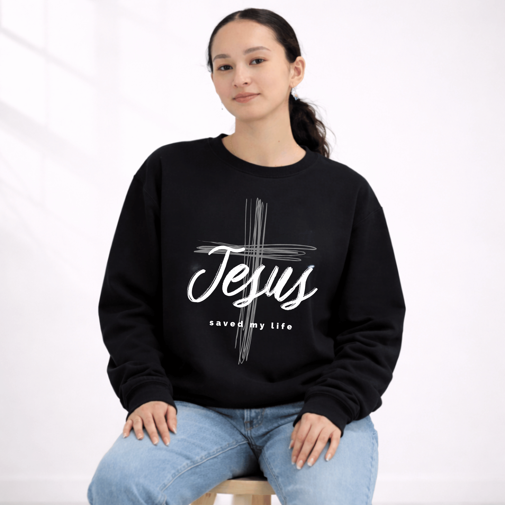 Person wearing a black sweatshirt with 'Jesus saved my life' design on a white background
