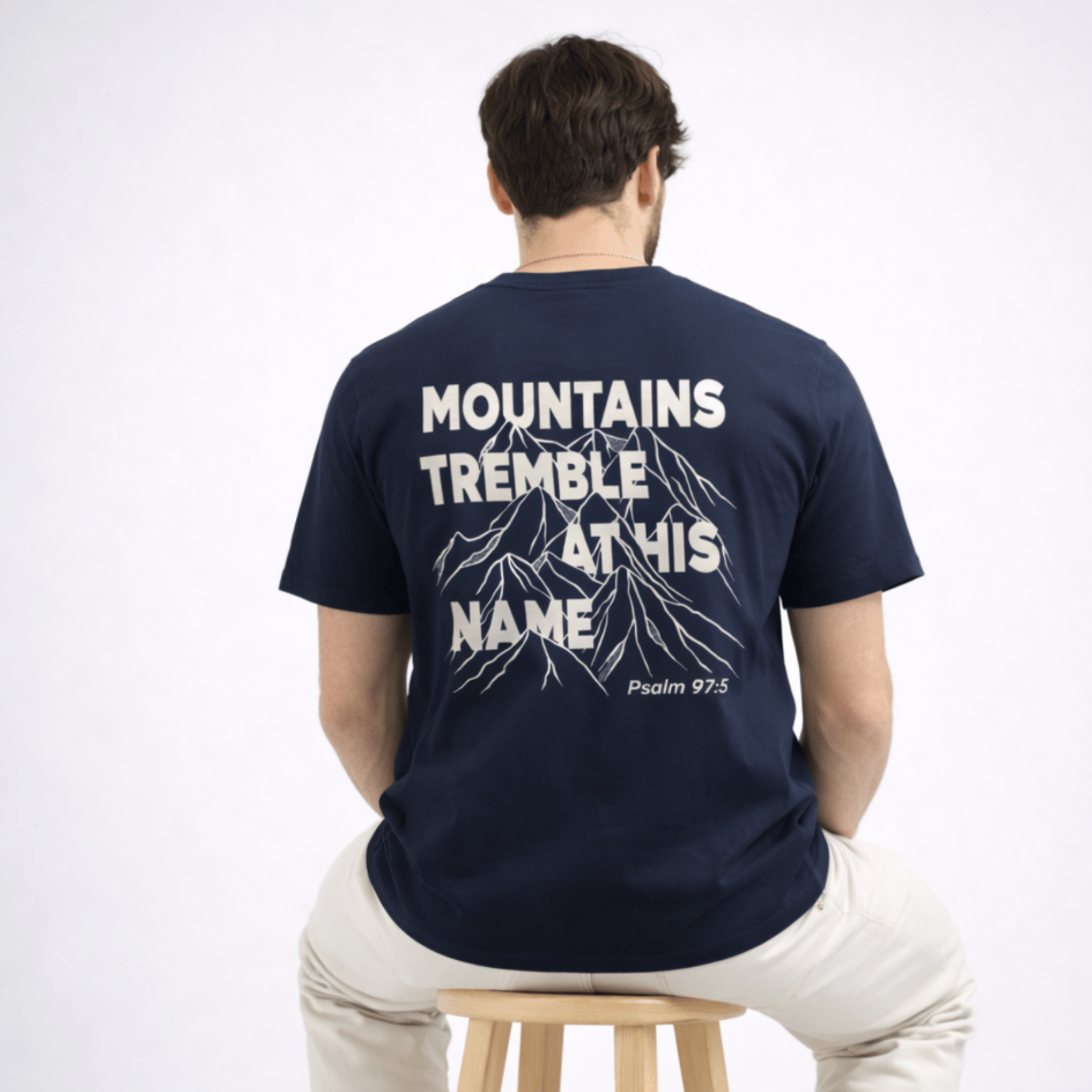 Person wearing a navy blue t-shirt with text and mountain graphic on the back, sitting on a stool.
