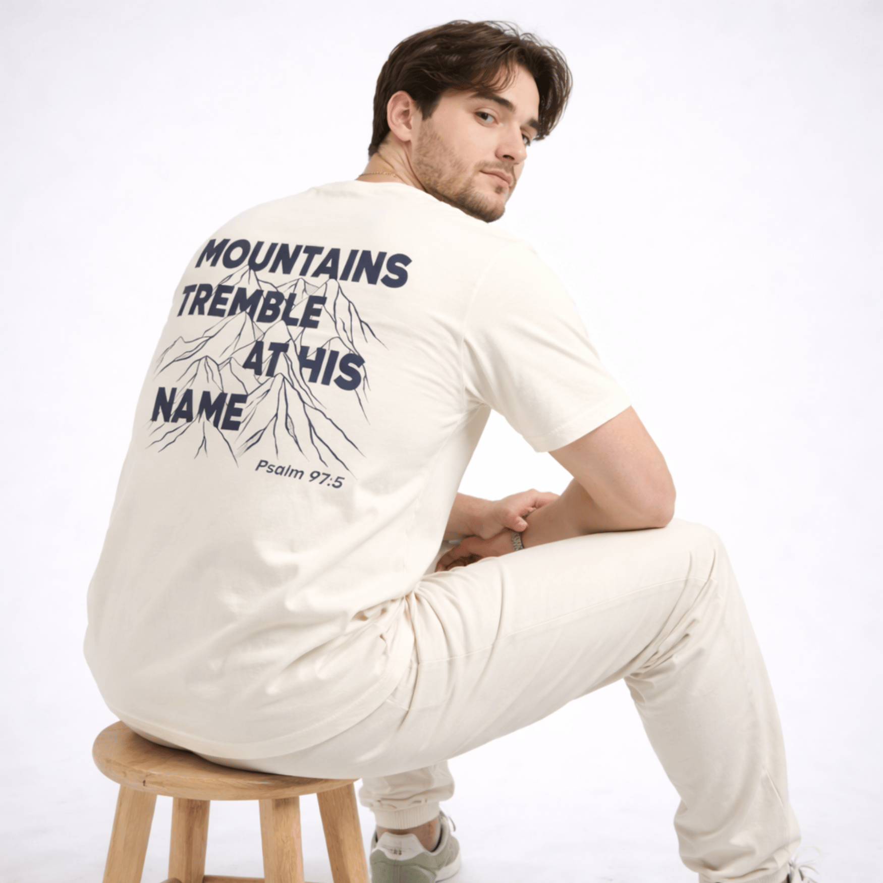 Man wearing a white long-sleeve shirt with text and graphics on the back, sitting on a wooden stool against a white background.