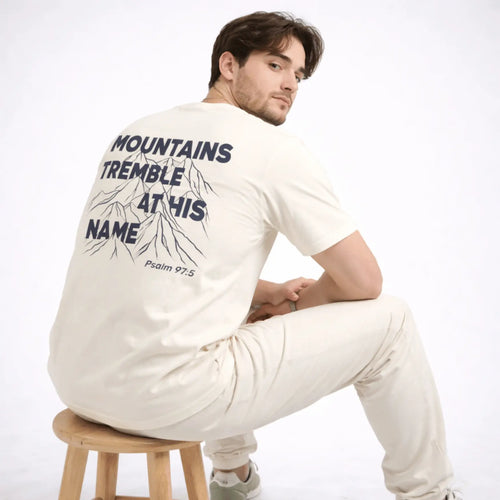 Man wearing a white long-sleeve shirt with text and graphics on the back, sitting on a wooden stool against a white background.