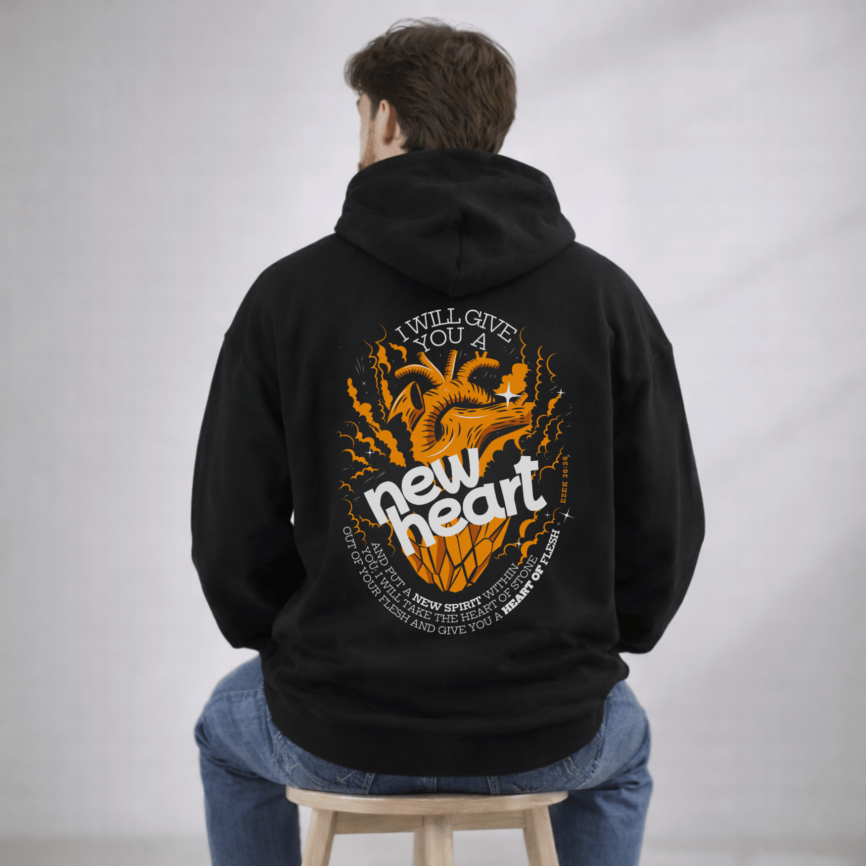 Person wearing a black hoodie with a graphic design on the back, sitting on a stool against a plain background.