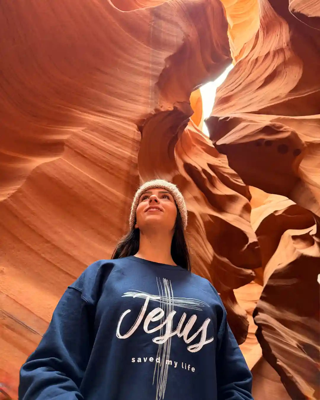 Person wearing a blue sweatshirt with 'Jesus saved my life' text in a desert canyon.