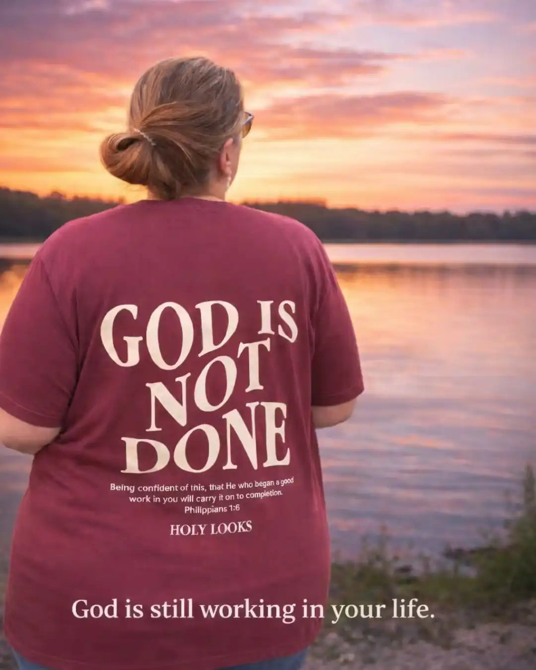 Person wearing a t-shirt with 'God is not done' text at sunset by a lake