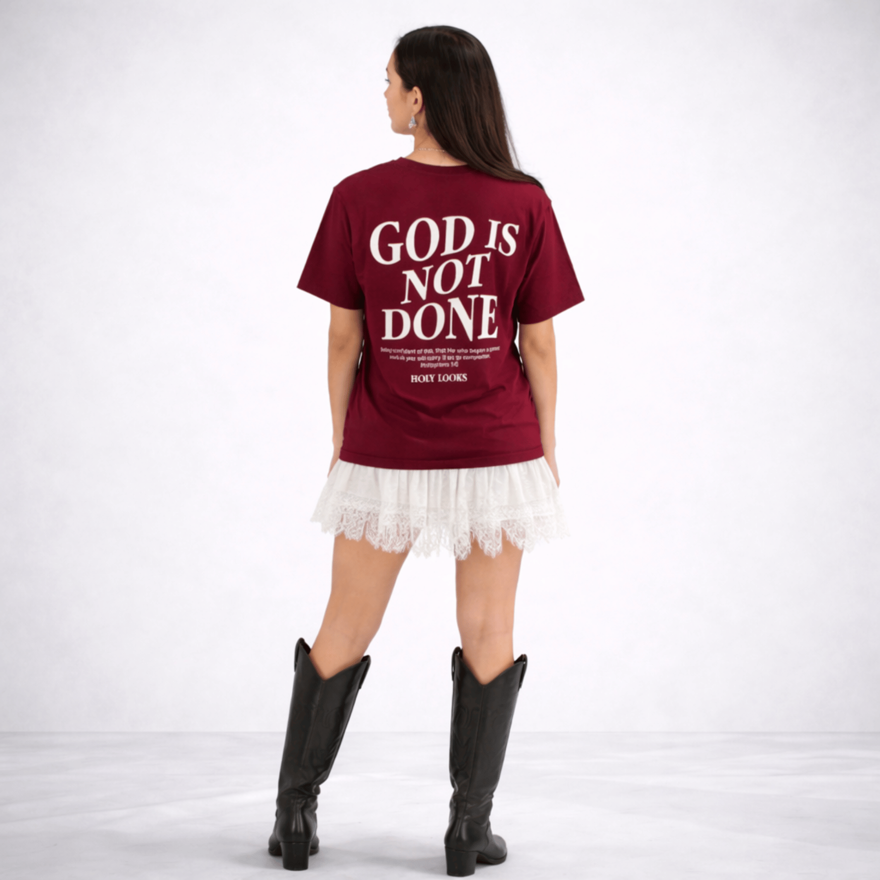 Person wearing a maroon t-shirt with 'GOD IS NOT DONE' text on the back, standing against a white background.