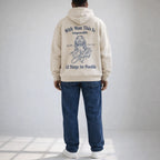 Person wearing a beige hoodie with text and a graphic of a religious figure on the back, standing against a plain background.