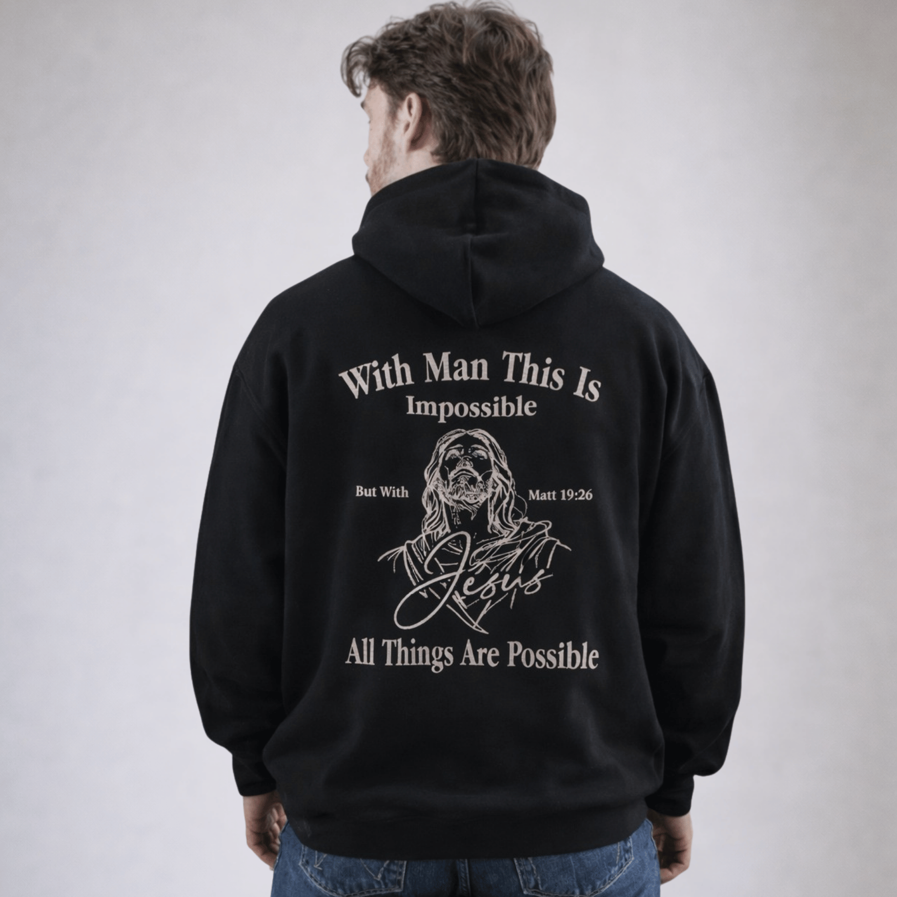 Person wearing a black hoodie with text and a graphic of Jesus on the back, on a plain background.