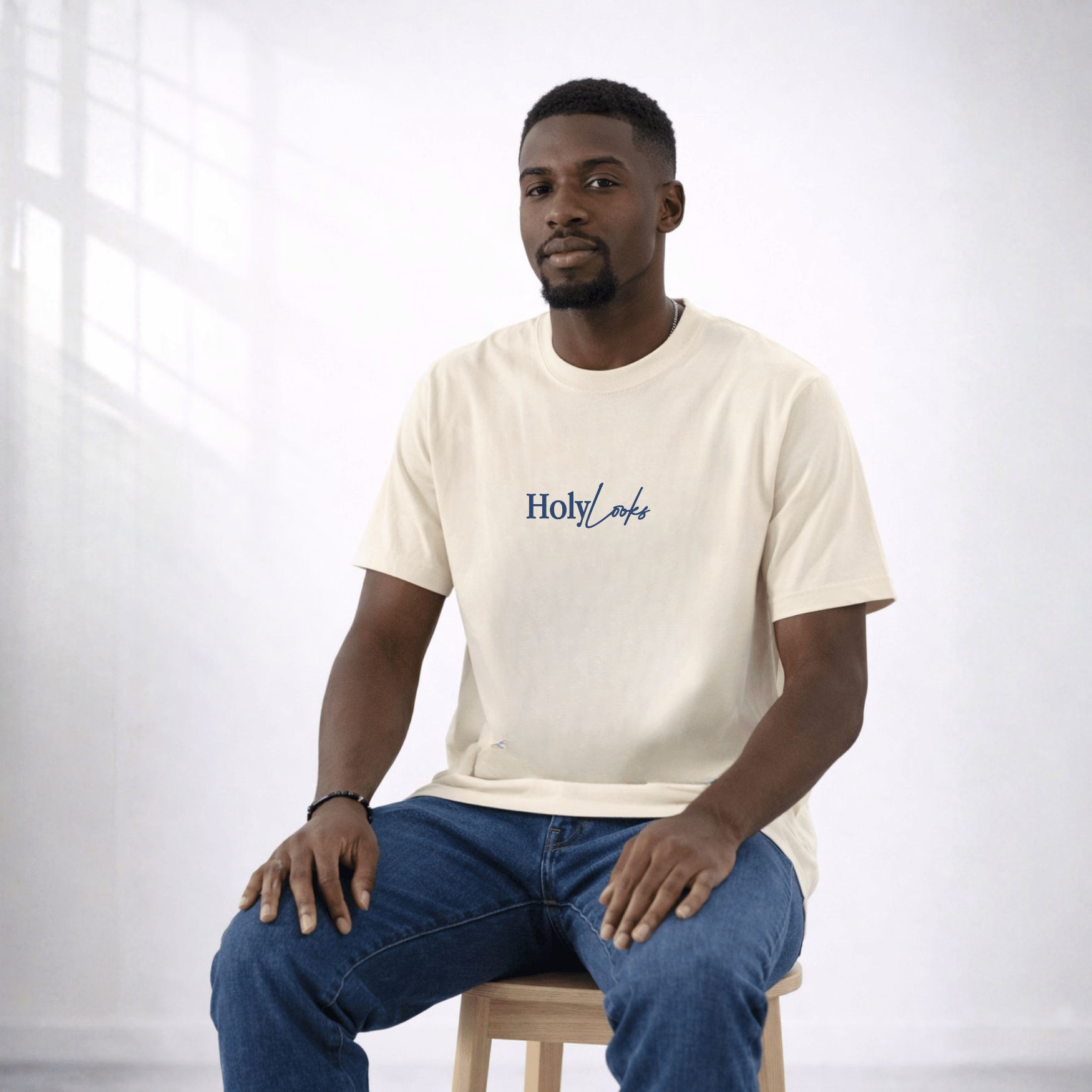 Man wearing a beige t-shirt with 'Holy Loaf' logo sitting on a stool against a white background