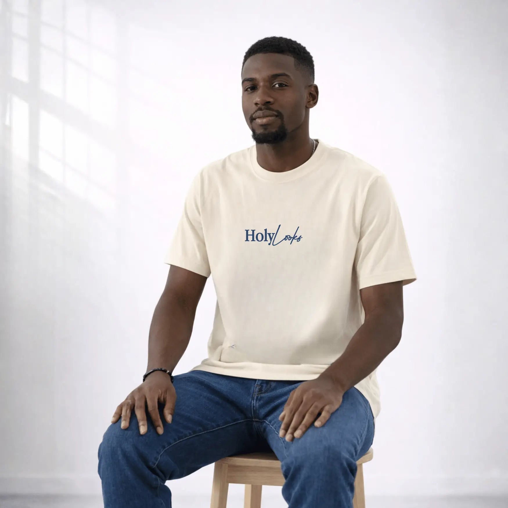 Man wearing a beige t-shirt with 'Holy Loaf' logo sitting on a stool against a white background