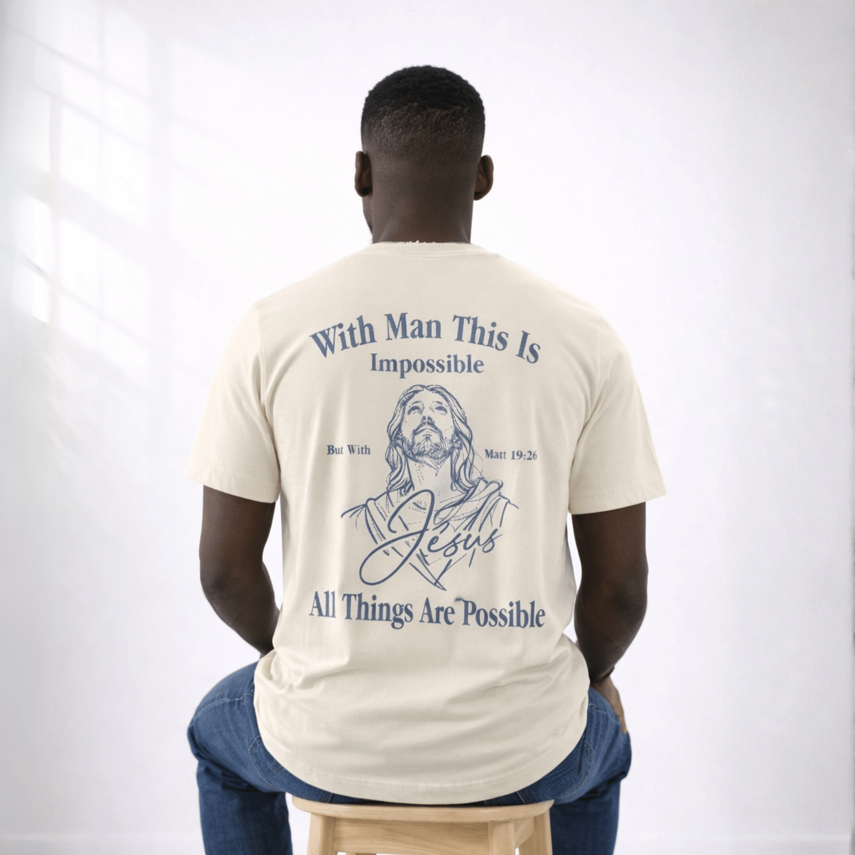 Man wearing a t-shirt with a Jesus illustration and text on the back, sitting on a stool against a white background.