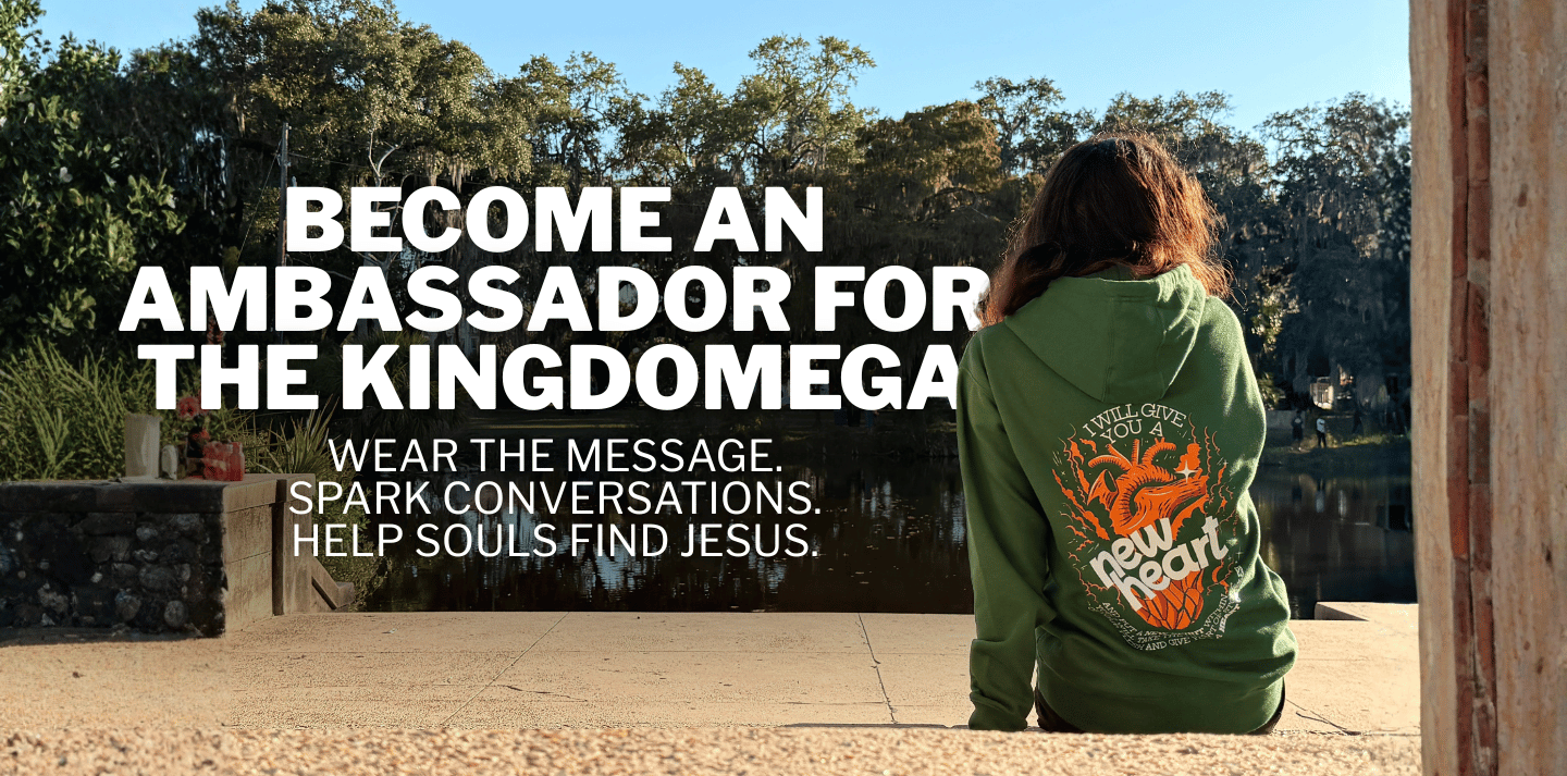 Person wearing a green hoodie with text and logo, sitting outdoors with trees in the background.