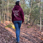 Person wearing a hoodie with 'God is not done' text walking through a forest.