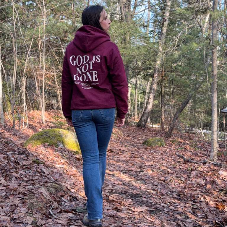 Person wearing a hoodie with 'God is not done' text walking through a forest.