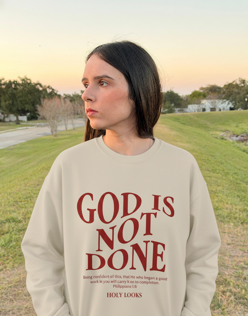 Person wearing a beige sweatshirt with 'God is not done' text in a park setting