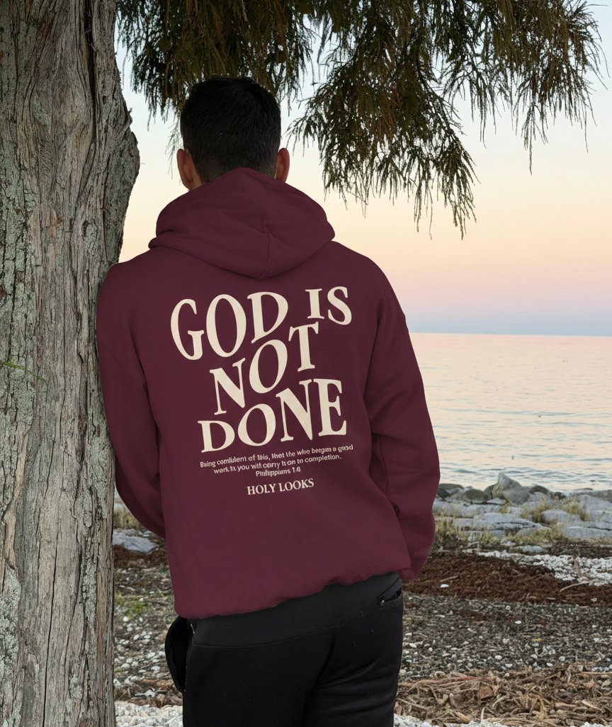Person wearing a maroon hoodie with 'GOD IS NOT DONE' text at the beach