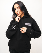 BLACK A woman wearing a black pullover hoodie with white text on the left chest reading 'Obedience is Worship' and a white cross graphic on the right sleeve, posed against a plain light background.