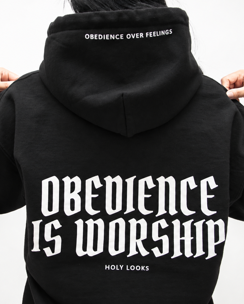 BLACK A person shown from the back wearing a black hoodie with large white gothic text reading 'Obedience is Worship' and smaller text 'Holy Looks' below, plus 'Obedience over Feelings' printed inside the hood.