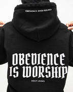 BLACK A person shown from the back wearing a black hoodie with large white gothic text reading 'Obedience is Worship' and smaller text 'Holy Looks' below, plus 'Obedience over Feelings' printed inside the hood.