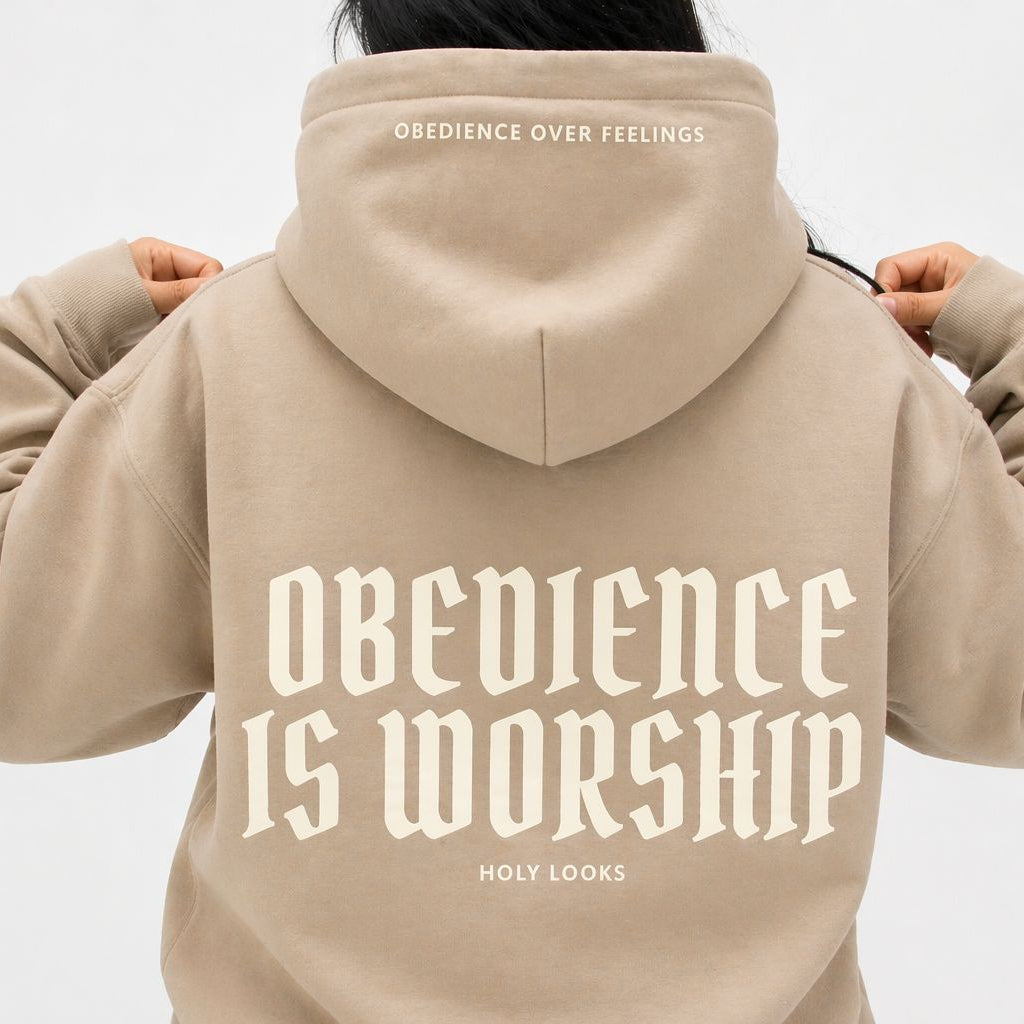 Beige hoodie with 'Obedience is Worship' text on the back, worn by a person against a light gray background.
