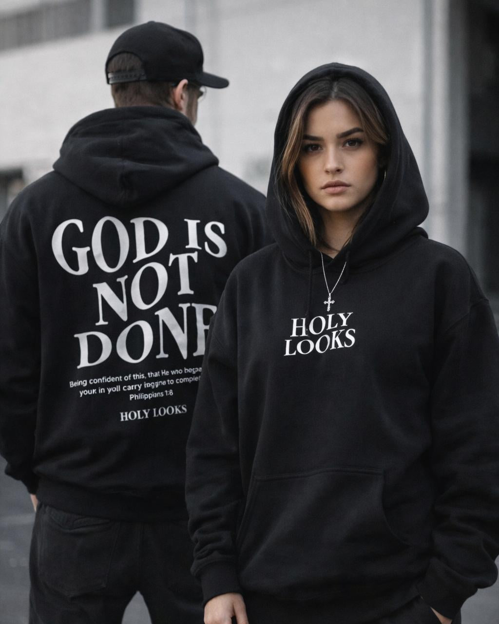 Two models wearing black hoodies with white text. The model in the foreground shows the front of a hoodie with 'HOLY LOOKS' printed on the chest.
